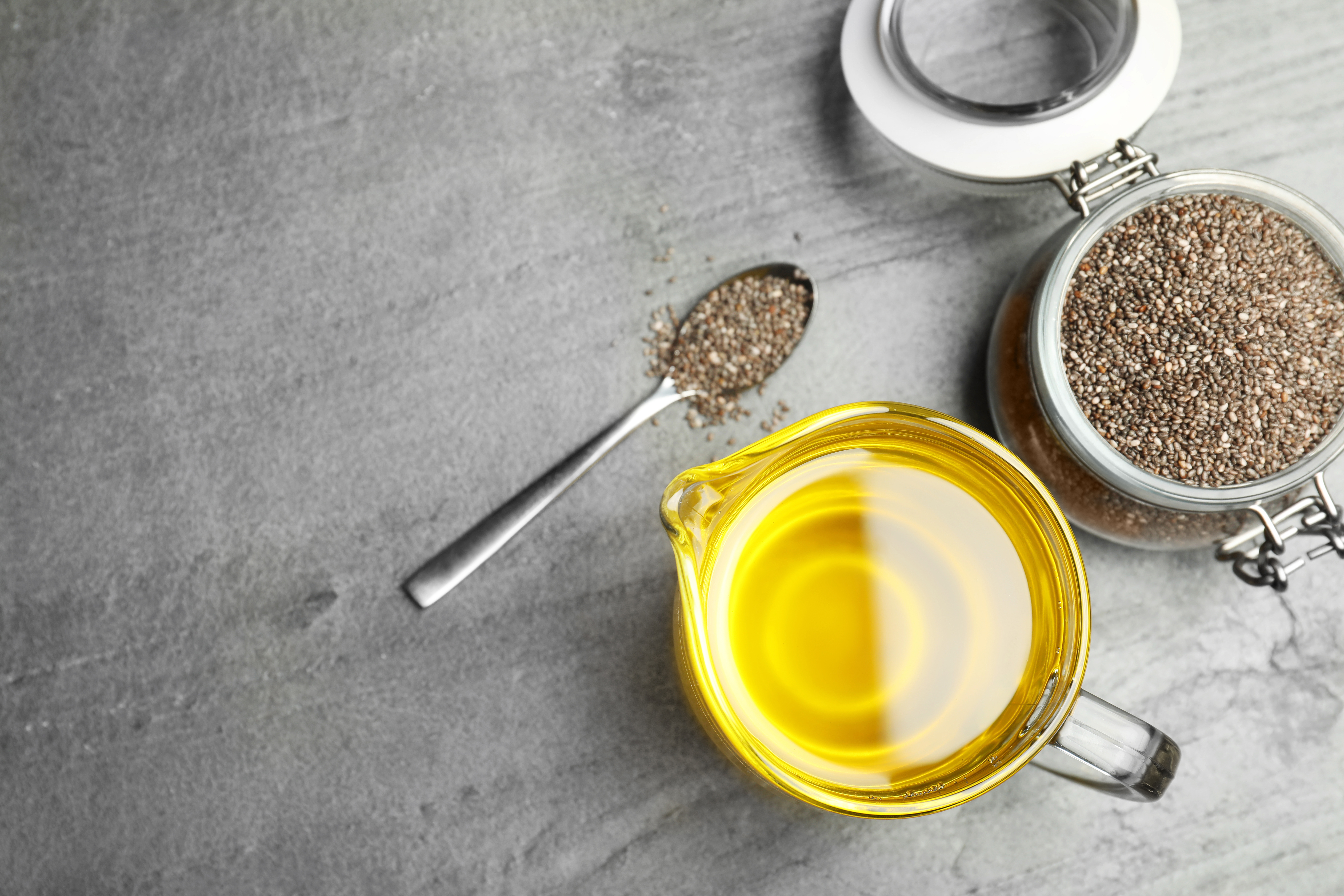 Flat lay composition with chia oil and seeds on grey background, space for text