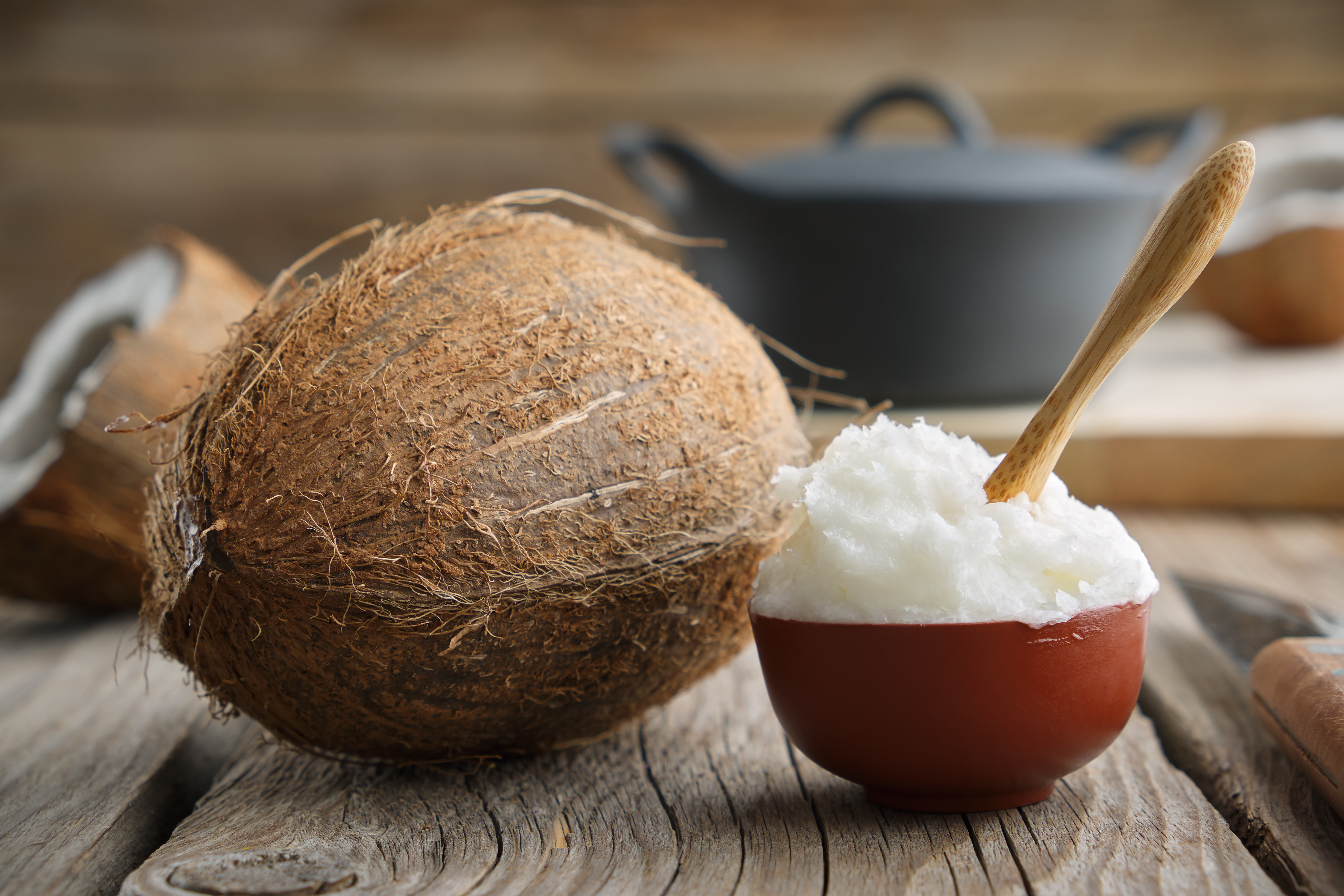Healthy coconut oil for cooking in ceramic bowl and coconuts on wooden kitchen table.